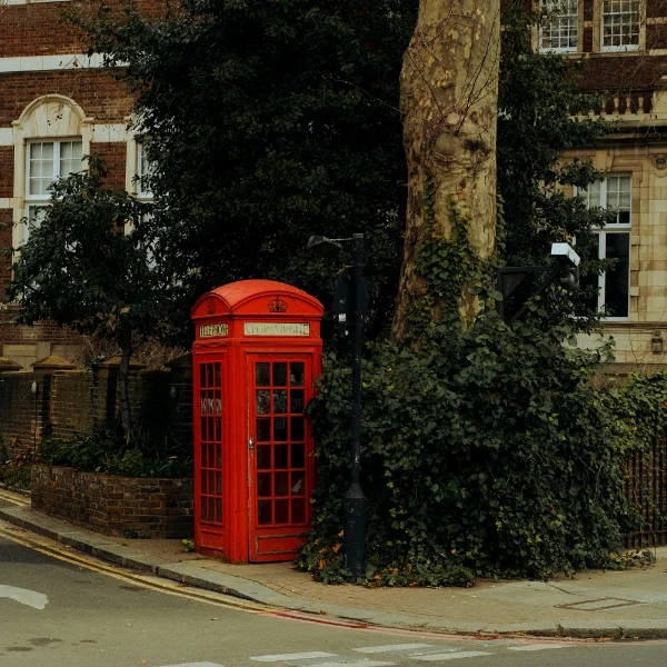 Vintage Red Telephone Box in London: Overgrown Greenery, Beige Brick Building, Victorian Lamppost