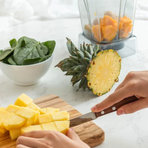 Someone cutting up pineapple and adding to a smoothie maker
